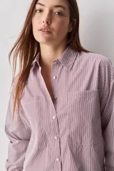 Camisa de calce relajado con diseño a rayas verticales en tonos azul y blanco, cuello clásico, mangas largas con puños abotonados y cierre frontal con botones. Presenta bolsillos aplicados en el delantero y una silueta versátil.