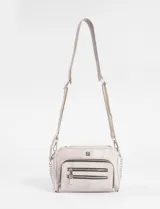 Bandolera negra de cuero vegano con correa ajustable y cadena lateral removible. Presenta un bolsillo frontal con doble cierre horizontal y un logo metálico cuadrado en la parte superior central.