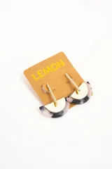Aros colgantes compuestos por una pieza semicircular de resina con patrón carey en tonos grises y blancos, combinada con un aplique metálico dorado de diseño geométrico.