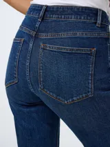 Jean de tiro alto con corte bootcut, confeccionado en denim azul oscuro. Presenta diseño de cinco bolsillos, cierre frontal con botón y cremallera, y terminación con tajos laterales en el ruedo.