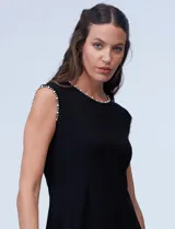 Vestido corto negro de seda fría, con escote a la base y mangas cortas. Apliques de perlas en escote y mangas.