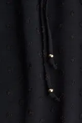 Pantalón negro de corte holgado y tiro alto, confeccionado en tejido plumeti (textura con pequeños puntos en relieve). Presenta cintura elástica fruncida con volados y cordón ajustable, además de bolsillos discretos en las costuras laterales.