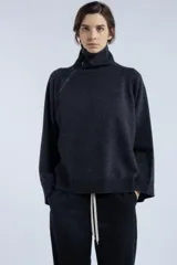Sweater gris oscuro de lana con cuello alto y cierre asimétrico en el hombro. Presenta un calce levemente amplio y caída fluida, mangas largas con terminaciones acanaladas y aberturas laterales.
