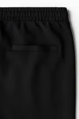Pantalón jogger negro de corte regular fit, confeccionado en tejido suave con mezcla de algodón. Presenta pliegues cosidos en la parte delantera, cintura elástica con cordón ajustable, bolsillos laterales y un bolsillo insertado en la parte trasera.