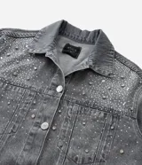 Campera de jean gris con efecto desteñido, corte oversized, cuello inglés, cierre frontal con botones niquelados y aplicaciones de brillos y piedras en la parte superior delantera.