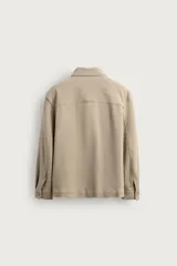 Sobrecamisa relaxed fit color beige con tejido elástico, cuello solapa, manga larga con puños abotonados, bolsillos de plastrón con solapa en el pecho, bolsillos laterales de vivo en la cadera y cierre frontal de botones.