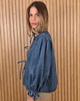 Camisa color beige de lino con mangas abullonadas tres cuartos y cierre frontal mediante múltiples lazos para atar.