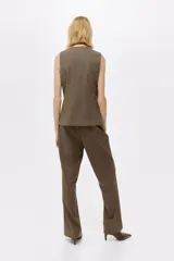 Chaleco largo de vestir color marrón oscuro, con cuello en V, cierre frontal de botones y bolsillos ribeteados. Presenta un corte entallado y abertura en la parte trasera.