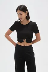 Top de manga corta con textura arrugada, cuello redondo y detalle de frunce frontal con argolla metálica y botón decorativo.