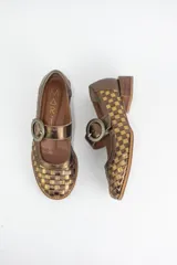 Zapato estilo Mary Jane confeccionado en cuero trenzado con diseño de damero en blanco y negro. Presenta una tira con hebilla circular en el empeine y un taco bajo cuadrado.