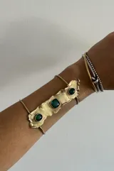 Brazalete rígido dorado con tres piedras verdes incrustadas.