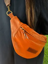 Riñonera de cuero vacuno color camel, con cierre principal y tirador de cuero, correa regulable y parche con logo grabado en el frente.