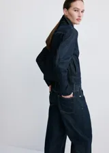 Chaqueta corta de denim en color azul oscuro, con cuello clásico, cierre frontal con botones, mangas largas y un bolsillo aplicado en el pecho.