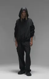 Campera rompevientos negra de calce oversize, confeccionada en microfibra técnica ligera con acabado semi-mate. Presenta capucha integrada, cierre frontal técnico y bolsillos tipo ojal. Destaca por su sistema de frunces elásticos regulables mediante tancas a lo largo de las mangas y el ruedo, permitiendo ajustar el volumen de la prenda.