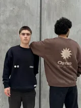 Buzo marrón con logo "Osten" y diseño gráfico de sol en color beige. Corte oversize, cuello redondo y mangas largas.