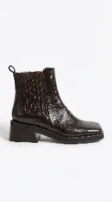 Bota tipo Chelsea de cuero con acabado brillante, diseño de punta cuadrada y elástico lateral. Cuenta con un taco de madera y suela de goma.