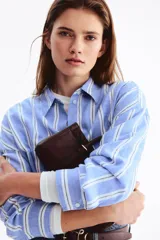 Camisa oversize confeccionada en mezcla de lino y viscosa, con diseño a rayas verticales en tonos celeste y blanco. Cuenta con cuello clásico, cierre frontal de botones, hombros caídos y mangas largas con puños abotonados.