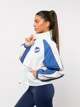 Campera deportiva Umbro del Club Nacional de Football, con diseño de bloques de color en azul marino y blanco. Presenta cuello alto, cierre frontal completo, bolsillos laterales y el escudo del club junto al logo de la marca en el pecho.