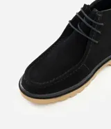 Bota tipo coturno de caña baja confeccionada en cuero gamuzado negro, con cierre de cordones, tirador en el talón y suela track de color tostado.