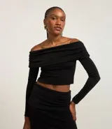 Blusa corta negra con escote bardot, mangas largas y canesú ancho con superficie metalizada.