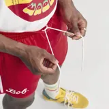 Short deportivo Adidas Originals en colaboración con Bob Marley, color rojo con las icónicas tres tiras blancas laterales. Presenta el nombre 'Bob' bordado en la pierna derecha y el logo del Trifolio en la izquierda.