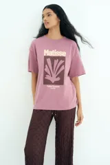 Remera de corte oversized en punto de algodón, con cuello redondo acanalado y mangas cortas de hombros caídos. Presenta un estampado frontal artístico con la inscripción Matisse y motivos abstractos.