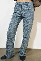 Pantalón jean tiro alto de corte flare con diseño jacquard estampado completo, cinco bolsillos, trabillas para cinto y cierre frontal con cremallera y botón metálico.