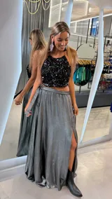 Pollera larga de satén plateado con acabado metalizado, corte evasé, cintura alta y tajo lateral profundo.