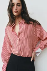 Camisa de cuello solapa y manga larga con rayas verticales rojas y blancas, con puños anchos blancos contrastantes y cierre frontal de botones.