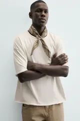 Camiseta de corte relajado (relaxed fit) color blanco roto, con cuello redondo y manga corta. Presenta un bordado sutil en el pecho con diseño floral en tonos claros.