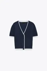 Chaqueta de punto de manga corta con escote en pico y cierre frontal con botones. Presenta un diseño en color azul marino con bordes en contraste de color blanco en el cuello, la tapeta de botones, los puños y el ruedo.