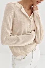 Jersey de punto color beige, con cuello redondo y cierre frontal parcial de botones, manga larga y acabados en rib.