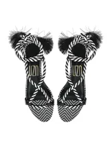 Sandalias planas con tiras de cuero negro y tobilleras de cordón trenzado en blanco y negro con borlas.