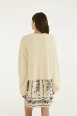 Cardigan básico de punto color marfil, con textura suave y esponjosa, cierre frontal de botones y mangas largas holgadas.