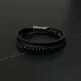 Pulsera triple de diseño multicapa, compuesta por una tira de cuero liso, una tira de cordón trenzado y una tira con pequeñas cuentas metálicas. Cuenta con un cierre magnético de acero inoxidable.