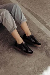 Zapatillas negras con paneles laterales de efecto piel de serpiente metalizado en tonos bronce y negro. Tienen cordones negros y suela de goma color caramelo.