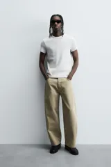 Camiseta de corte relajado, color gris claro, confeccionada en tejido con estructura waffle. Presenta cuello redondo y manga corta, con costuras decorativas en contraste color dorado que recorren los laterales y los hombros.