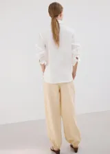 Camisa de lino blanca de corte recto, con cuello camisero, mangas largas y cierre frontal oculto de botones.