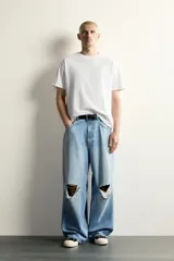 Jeans baggy fit de corte holgado en denim de algodón celeste, con tiro medio, cinco bolsillos, roturas en las rodillas y cierre frontal con cremallera y botón.