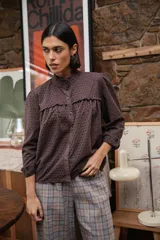 Camisa de broderie color chocolate, con cuello alto con volados, cierre frontal de botones y mangas largas con volumen.