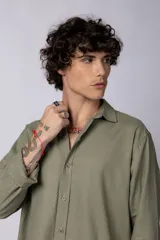 Camisa de manga larga confeccionada en lino, color verde oliva, con cuello clásico y cierre frontal de botones.