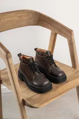 Borcegos de punta cuadrada con diseño acordonado, combinando paneles de cuero texturizado y gamuza en tonos marrones. Presentan una suela track gruesa de goma negra y cordones negros.