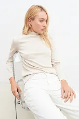 Blusa beige claro con cuello alto y mangas largas, con pequeños brillos.