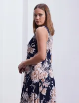 Vestido largo de seda fría con estampado floral en tonos beige y blanco sobre fondo azul marino. Tiene cuello redondo cruzado con abertura y aplique metálico.