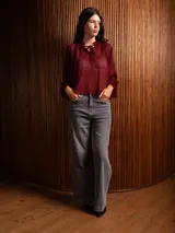 Blusa de plumeti color bordó, con cuello alto ajustable mediante lazo, mangas largas con puños elásticos y detalle de volados en las terminaciones.