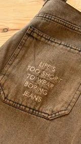 Jean balloon color marrón con efecto acid wash, corte ancho y tiro medio. Presenta un bolsillo trasero con el texto estampado "Life's too short to wear boring jeans" y etiqueta blanca en la pretina.