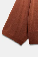 Jersey de punto color terracota, con cuello redondo y mangas amplias tipo murciélago.