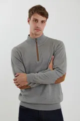 Sweater de punto gris con medio cierre frontal, cuello alto y coderas en tono marrón. Presenta un diseño clásico con puños y ruedo acanalados.