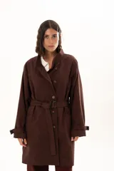 Trench color chocolate con cuello alto, cierre frontal con botones y cinturón ajustable en la cintura. Presenta mangas largas con puños ajustables mediante tiras y hebillas, y bolsillos frontales.