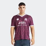 Camiseta de fútbol del Olympique de Marseille, color bordó con estampado geométrico en tonos oscuros. Presenta cuello polo blanco con detalles en negro, mangas cortas con borde blanco y logos estampados en el frente.